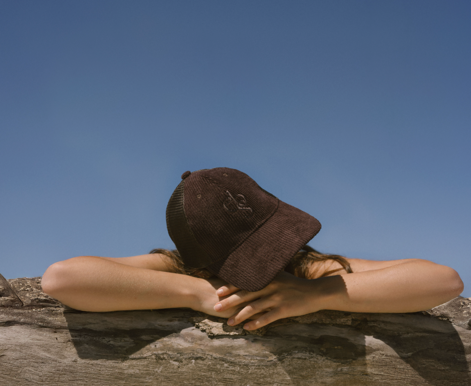 Person wearing Eco By Sonya Good Thoughts Cap on a rock with a clear blue sky in the background