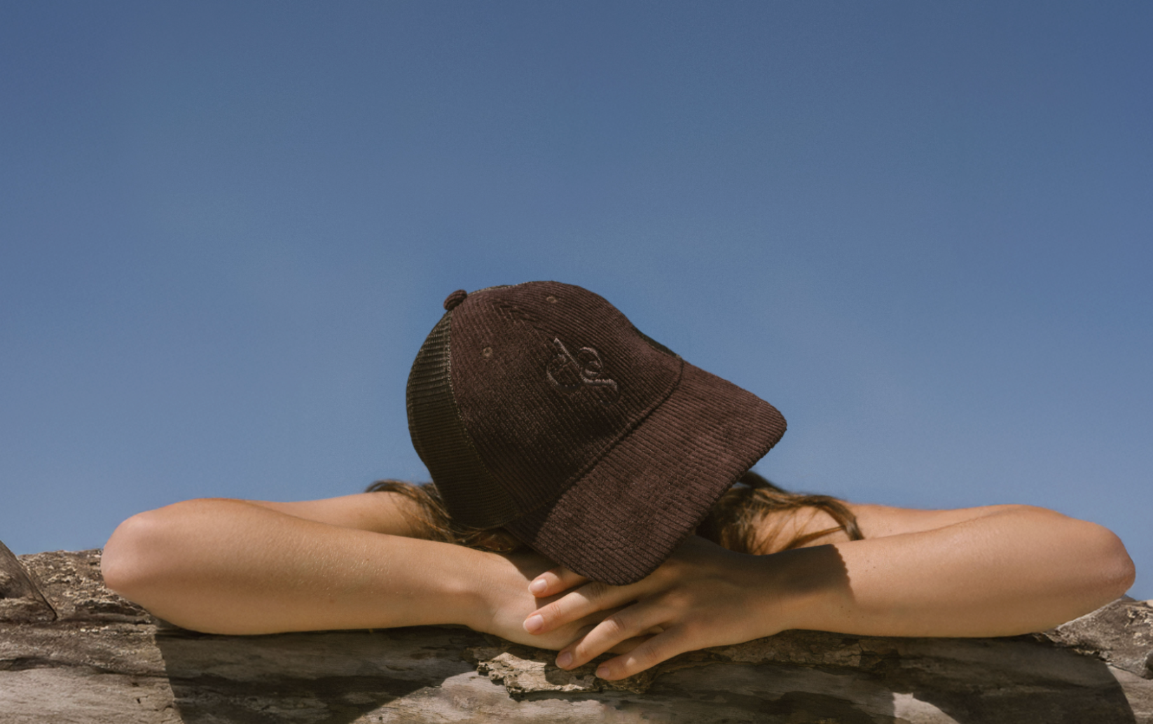 Person wearing Eco By Sonya Good Thoughts Cap on a rock with a clear blue sky in the background