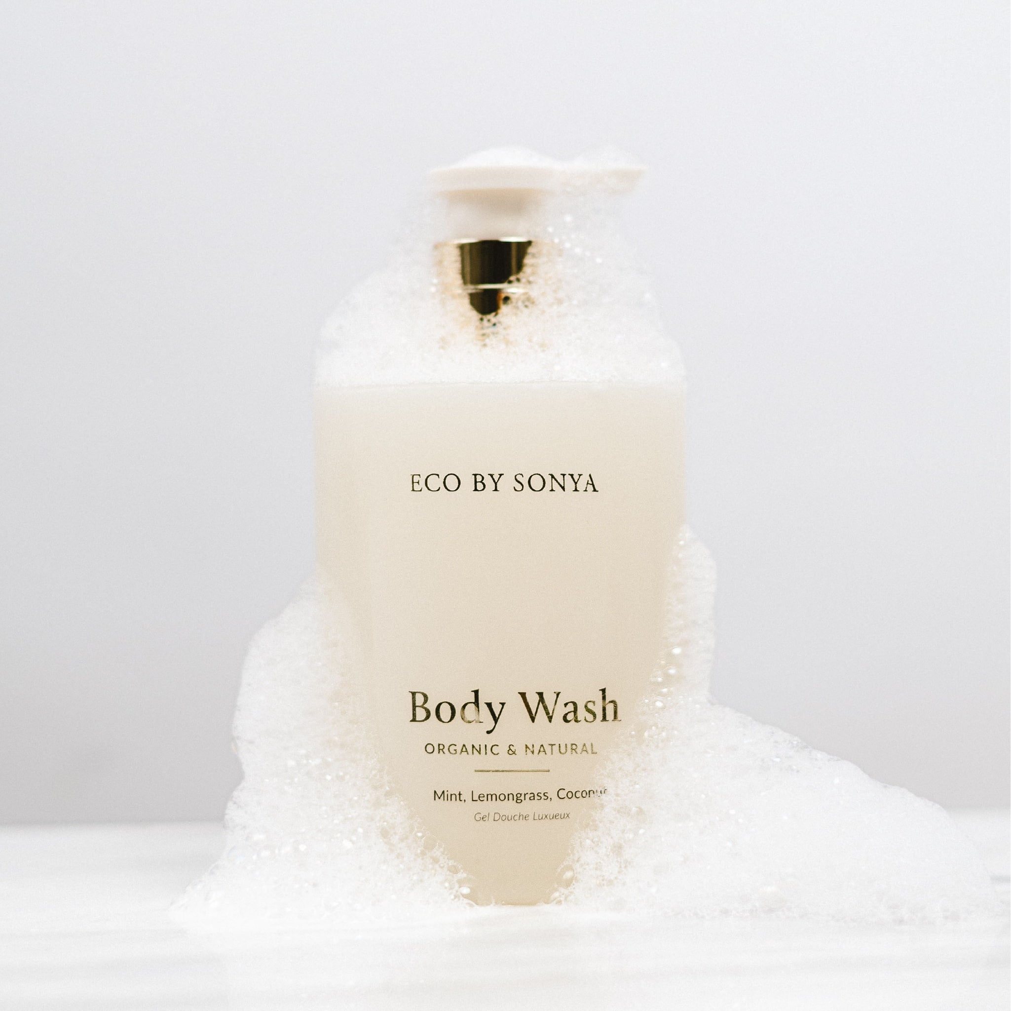 ECO BY SONYA Body Wash bottle surrounded by white foam against a clean white background.