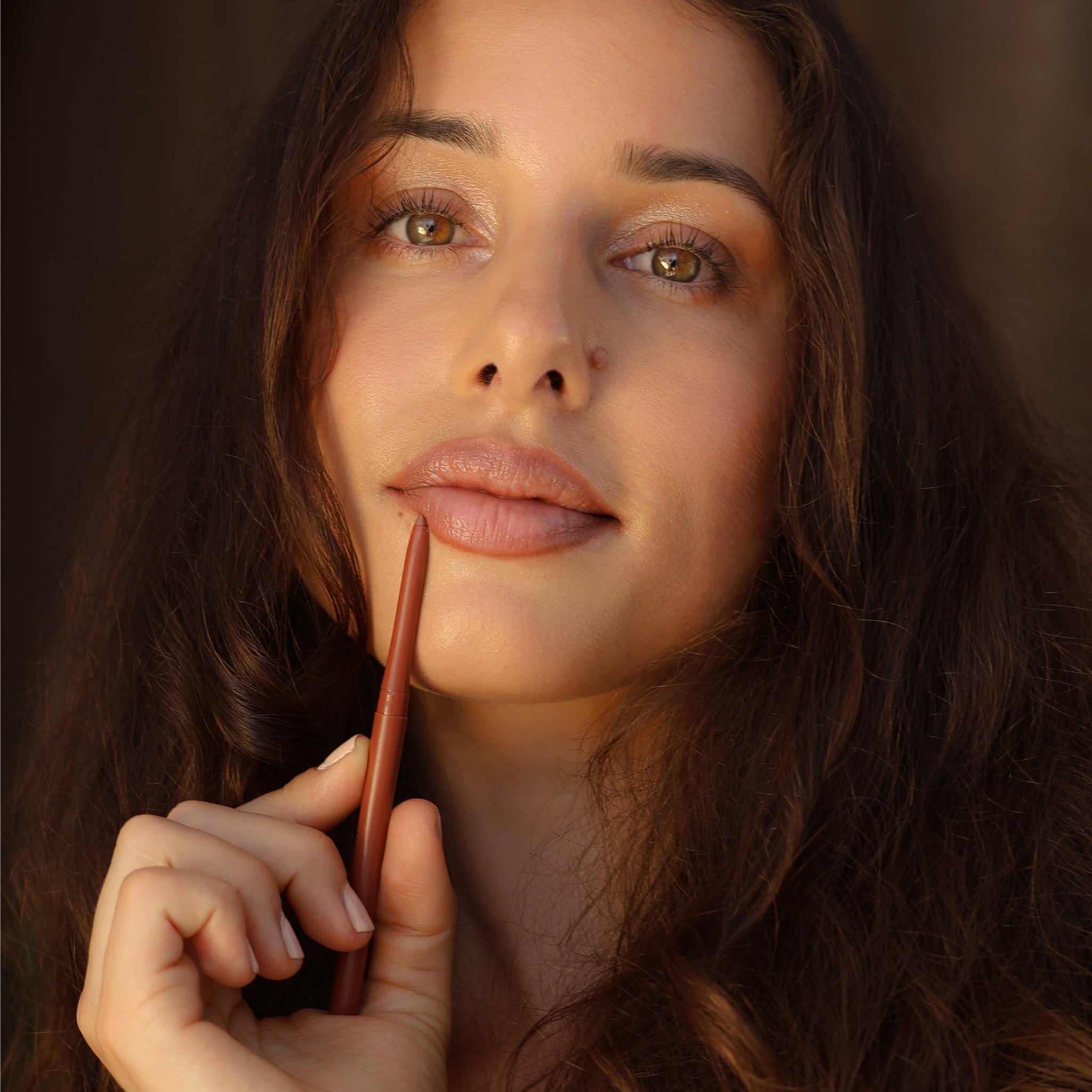 Portrait of a woman holding an Eco By Sonya Moody Nude lip liner near her lips.