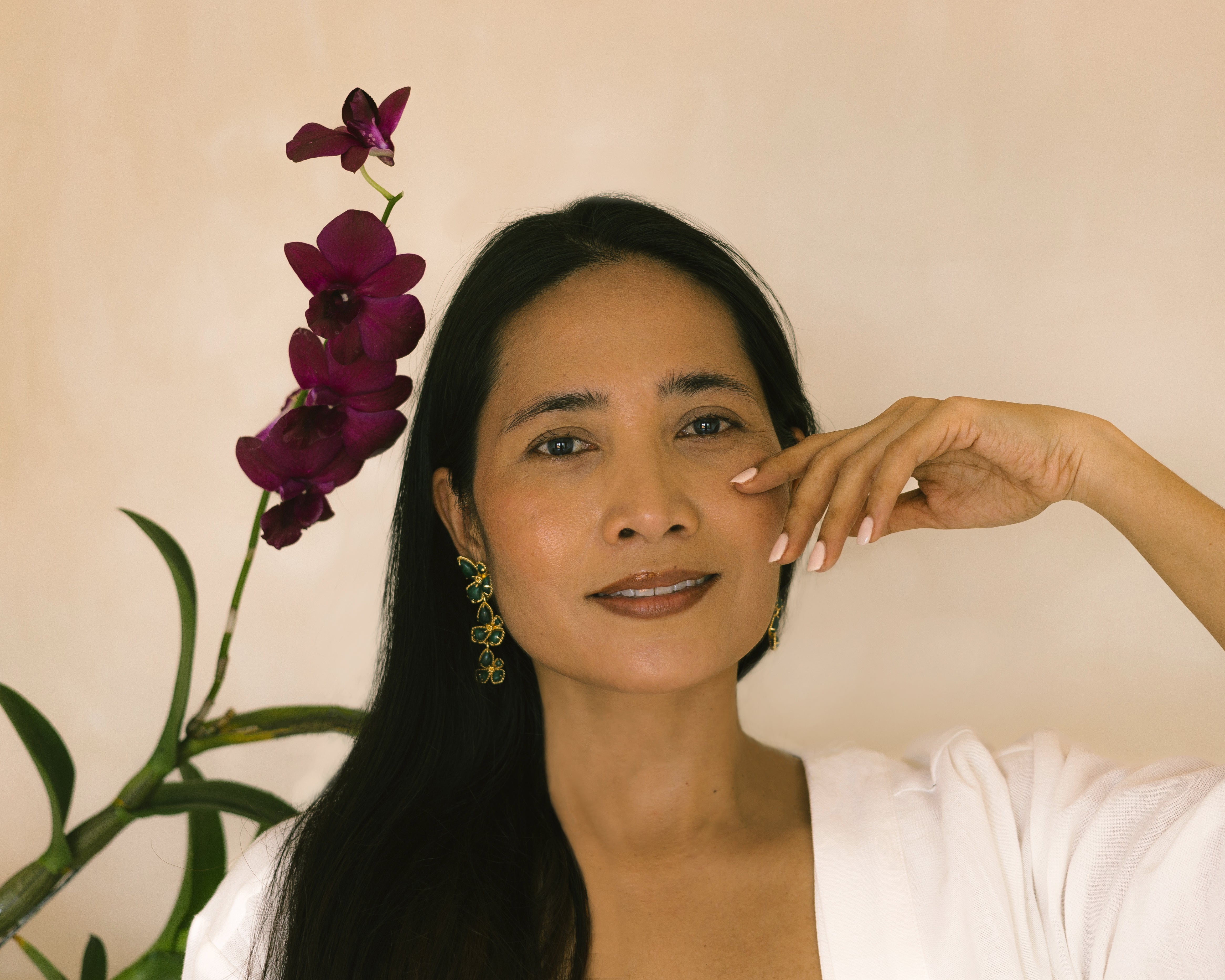 Woman with beautiful skin next to a flower against a beige background