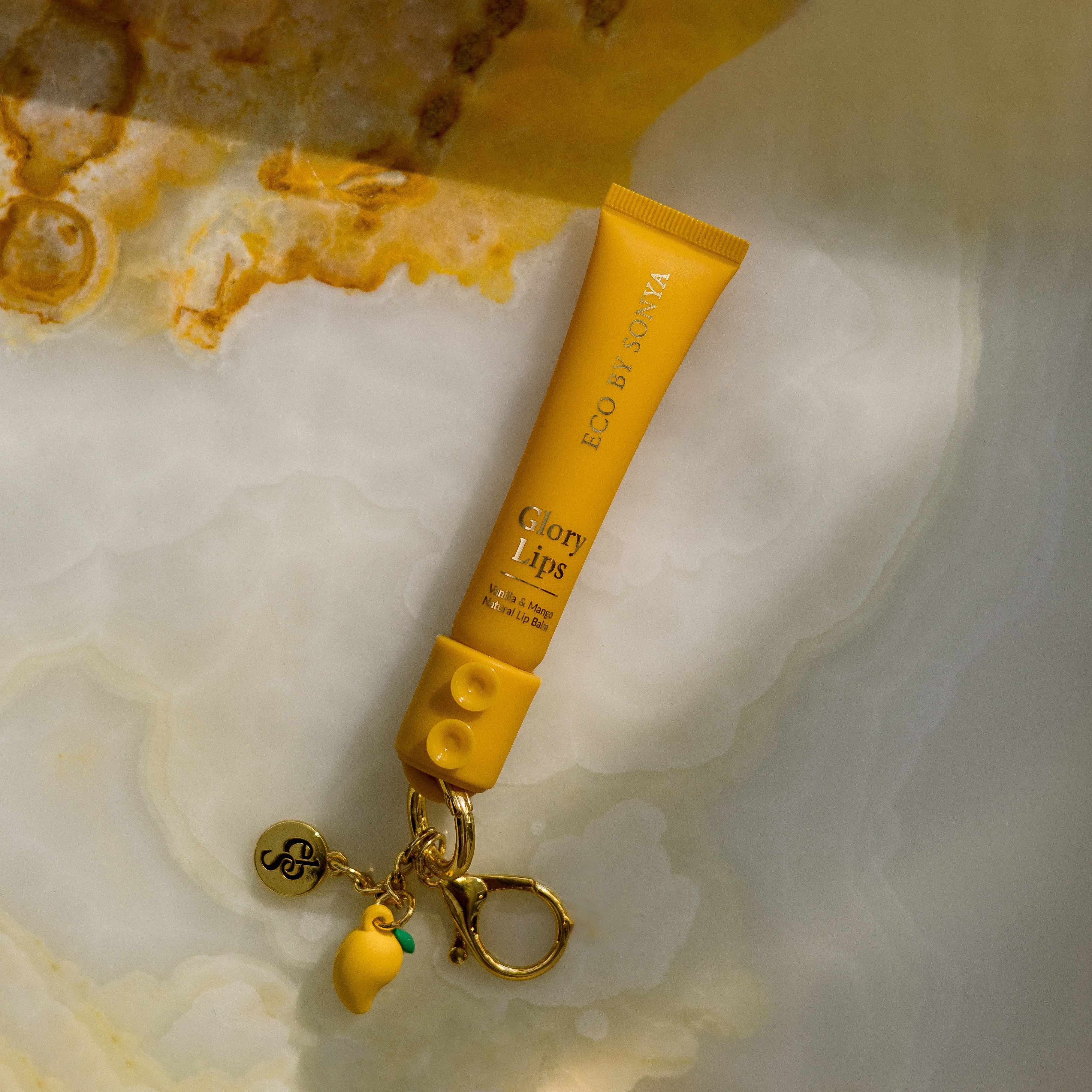 Yellow Glory Lips lip balm with a keychain on a marble surface