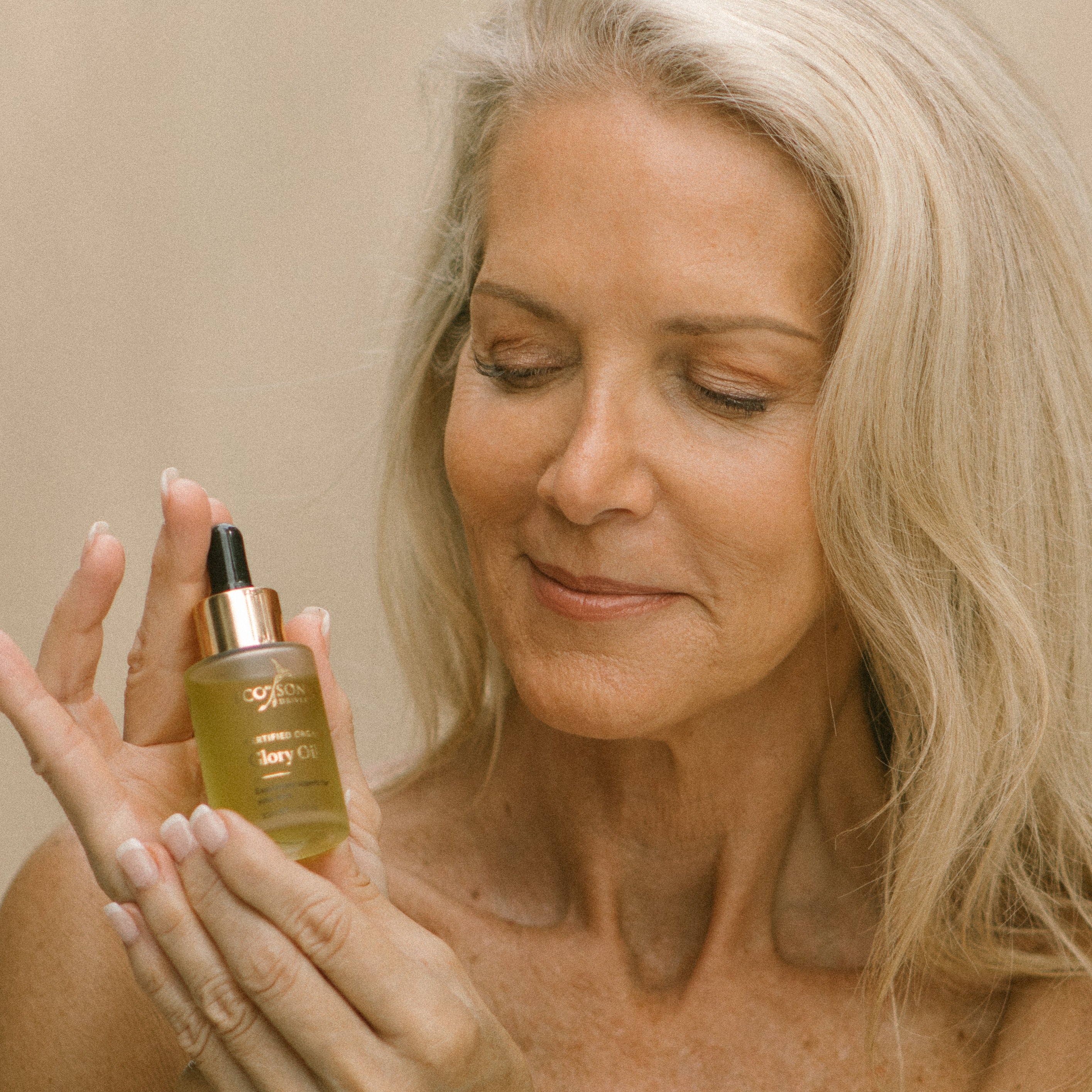 Mature woman with beautiful skin holding a bottle of Glory Oil