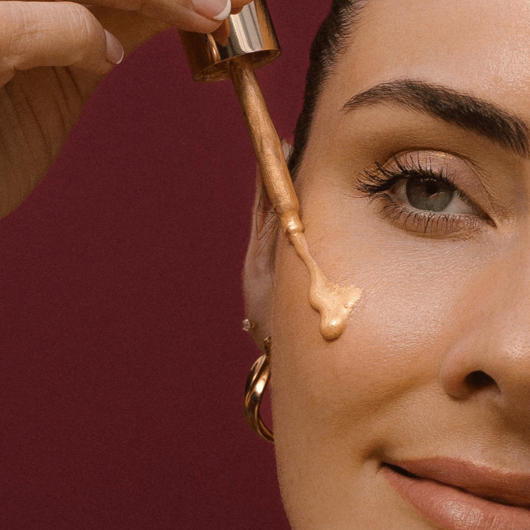 Close-up of a woman applying drops of Golden Illuminiser to her face with a dropper.