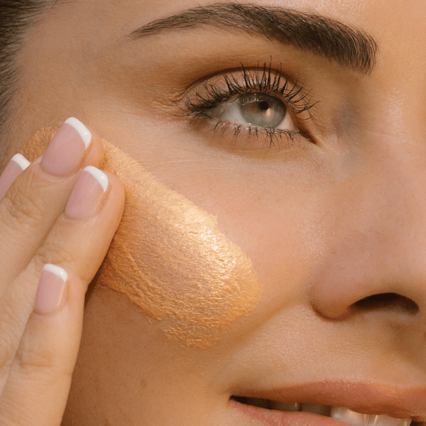 Close-up of a person applying Golden Illuminiser to their face with a finger.
