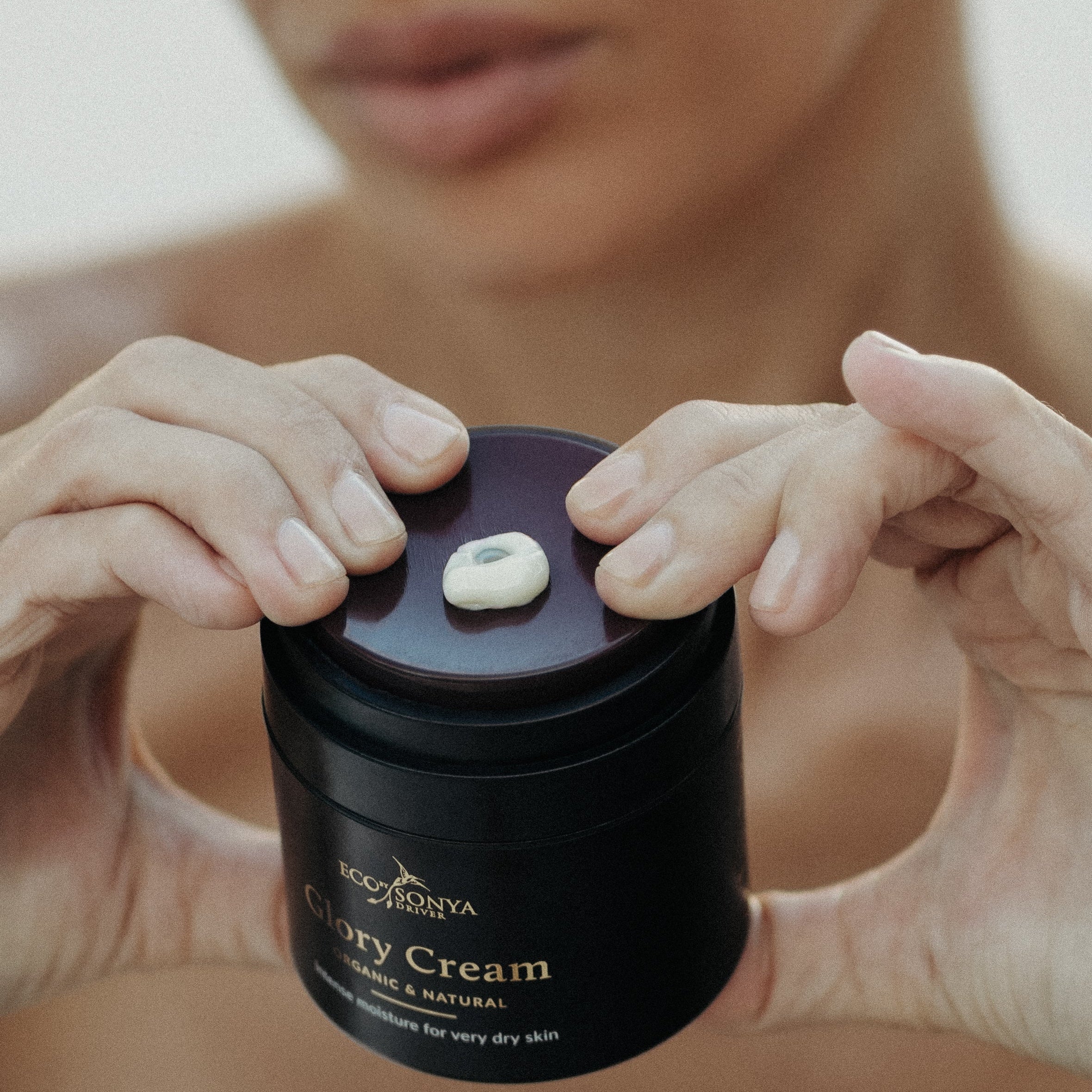 Person squeezing Eco By Sonya Glory Cream using the pump in the jar