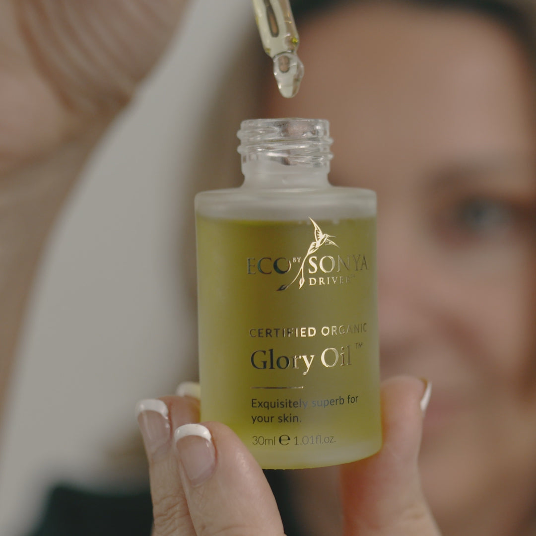 Woman using Eco By Sonya Glory Oil with golden dropper, applying golden face oil to cheeks and forehead with gentle tapping motions.